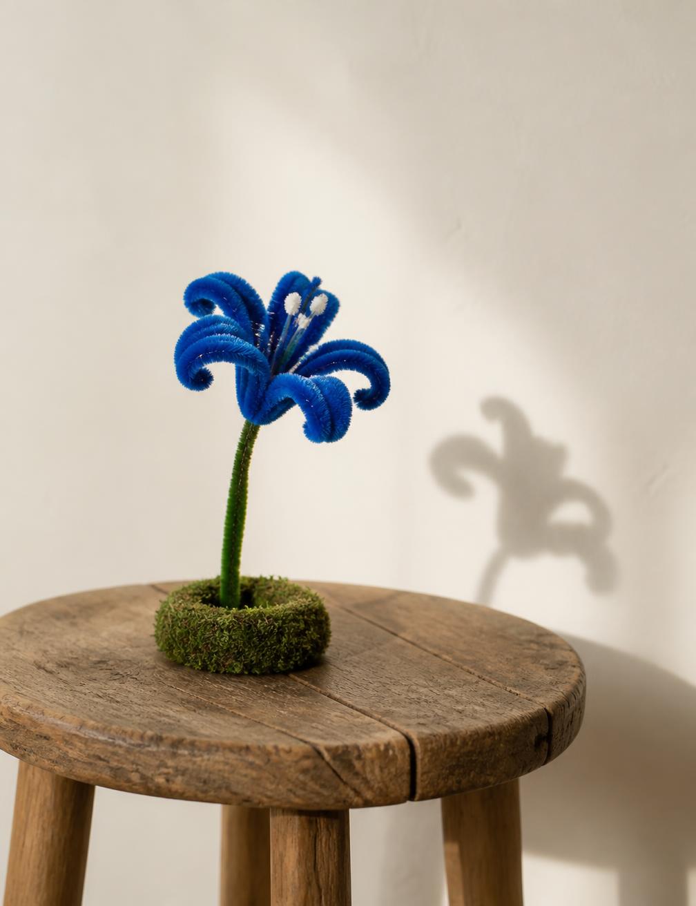 Single blue handmade pipe cleaner lily on a wooden stool